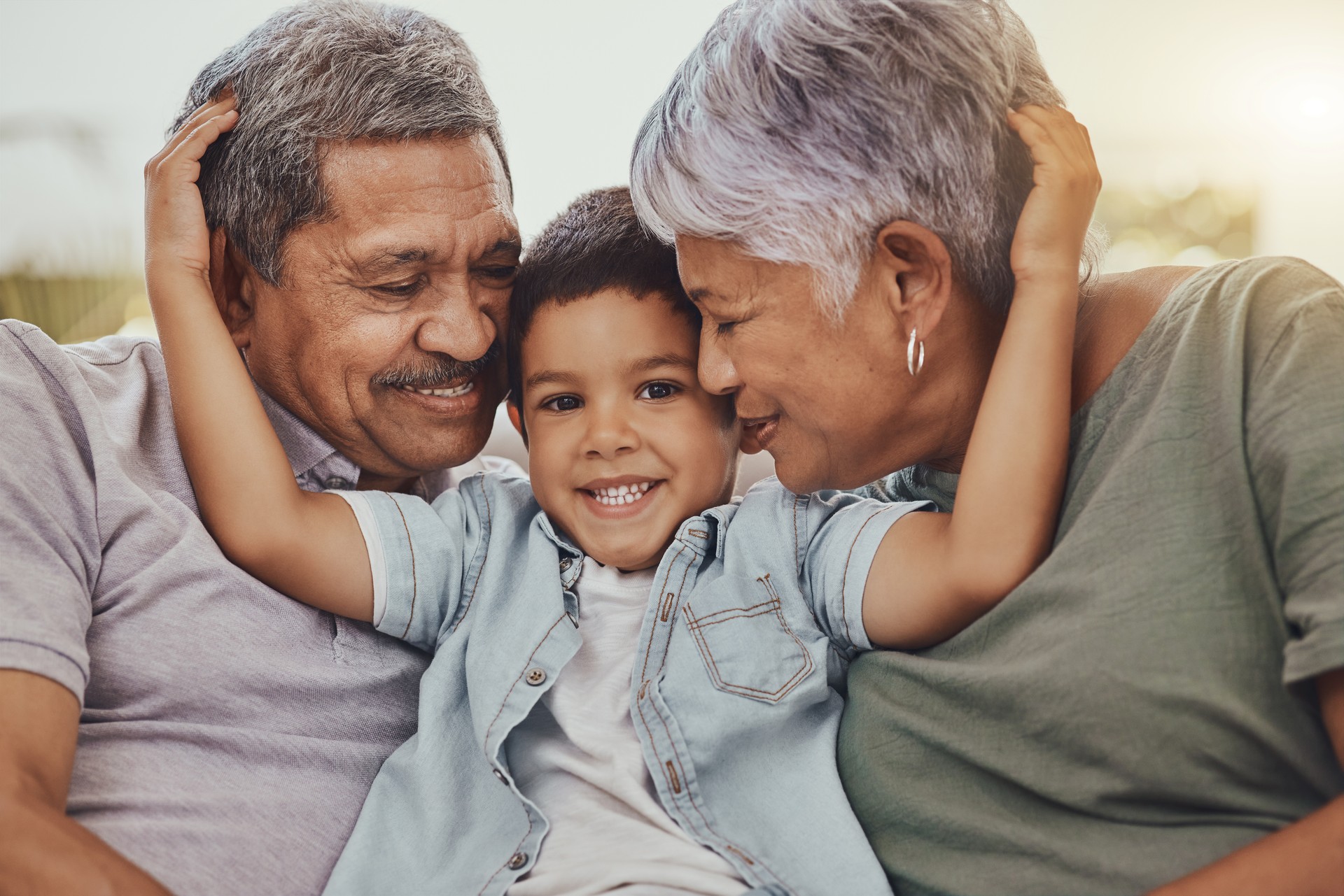 Family, portrait and child with grandparents in a living room, hug and happy, love and sweet while bonding in their home. Embrace, grandchild and grandmother with grandfather in a lounge hugging